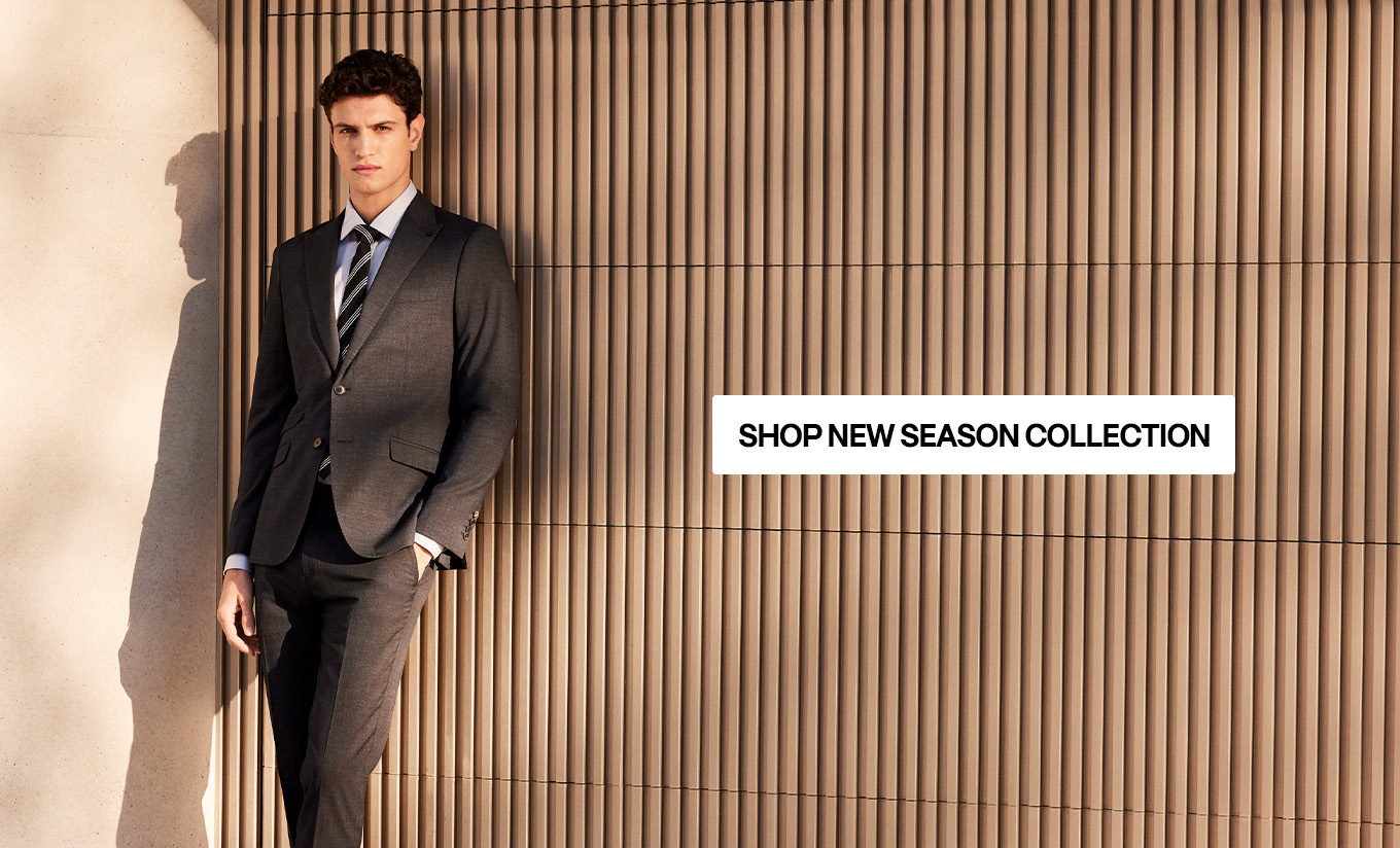 Model in POLITIX Spring Summer 2025 charcoal tailored suit with striped tie, styled against modern architecture – shop new season men’s suits and tailoring